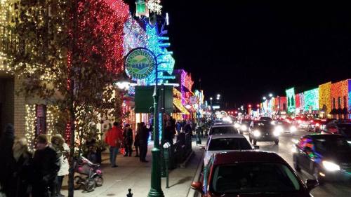 A festive street at night, adorned with colorful holiday lights, bustling with people and cars.