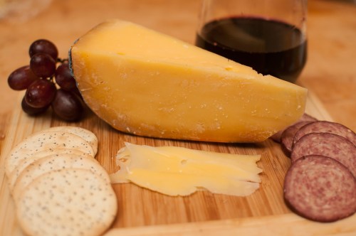A wooden board with cheese, crackers, salami, grapes, and a glass of red wine.