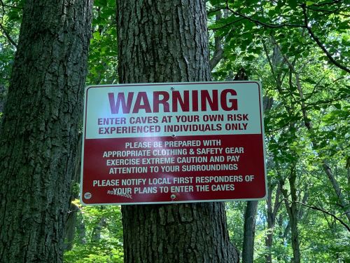 A warning sign on a tree advises entering caves at your own risk, for experienced individuals only, with safety precautions.
