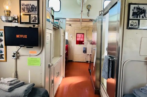 Interior of a train car featuring a Netflix screen, towels, and vintage photos on the walls.