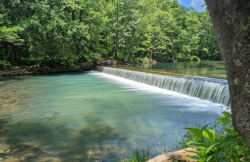 A serene waterfall cascading into a clear, tranquil pool surrounded by lush green trees.
