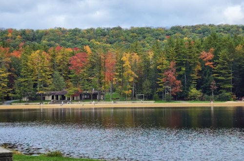 A serene lake surrounded by vibrant autumn foliage and a sandy beach, with people enjoying the outdoors.