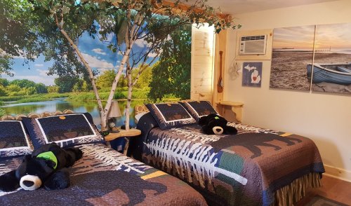 Cozy bedroom with two beds, bear-themed decor, and a nature mural featuring a river and trees.