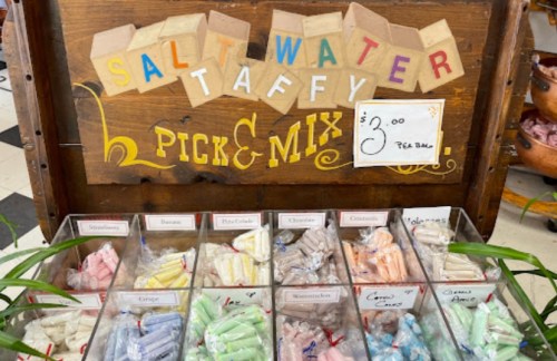 A wooden display with a sign reading "Salt Water Taffy Pick & Mix" and various colorful taffy candies in clear containers.
