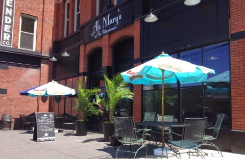 Outdoor seating area of Ale Mary's, featuring colorful umbrellas and potted plants against a brick building backdrop.