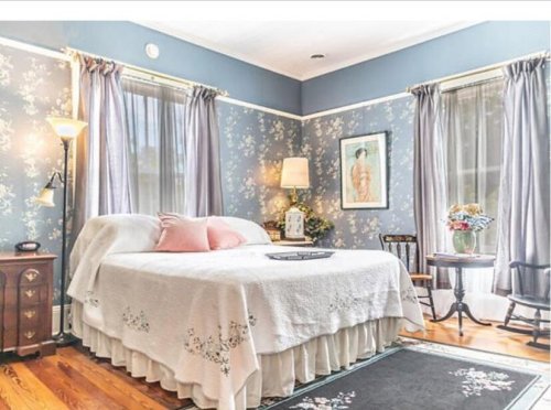 Cozy bedroom with floral wallpaper, a bed with a quilt, and a small table by the window. Soft lighting enhances the ambiance.