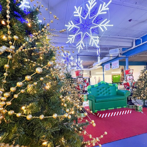 A festive scene with decorated Christmas trees, snowflake lights, and a green couch surrounded by holiday decorations.