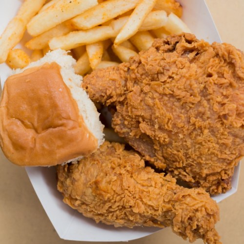 A serving of fried chicken with two pieces, a soft bun, and a side of crispy French fries in a takeout container.