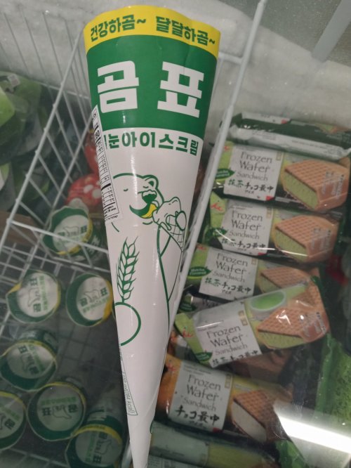 A cone-shaped ice cream package with a cartoon character, surrounded by various frozen snacks in a display freezer.