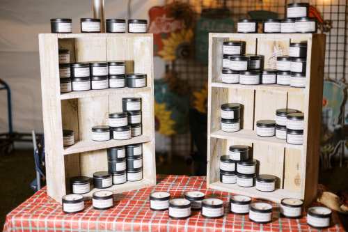Two wooden shelves filled with small black-lidded jars, displayed on a checkered tablecloth at a market.