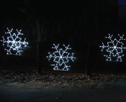 Three illuminated snowflake decorations on a wooden fence, glowing brightly against a dark background.