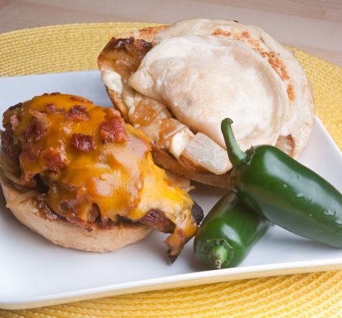 A plate with two sandwich halves: one topped with melted cheese and bacon, the other with peanut butter, plus two jalapeños.