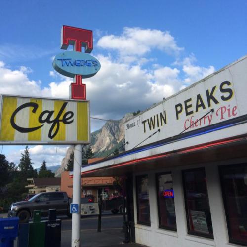 Sign for Tweed's Cafe, home of Twin Peaks Cherry Pie, with mountains in the background and a blue sky.