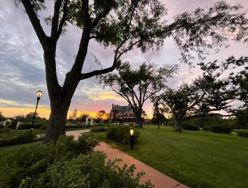 A scenic view of a park at sunset, featuring trees, a path, and a historic house in the background.