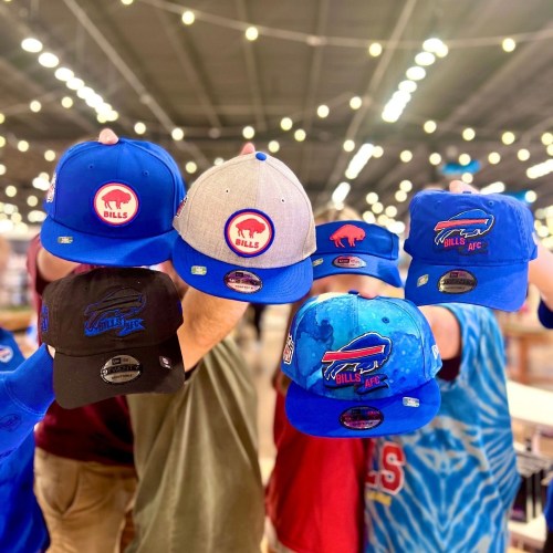A collection of Buffalo Bills hats in various colors and styles, held up against a blurred background of lights.