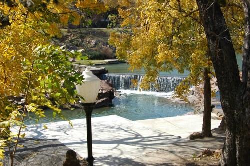 A serene scene of a small waterfall surrounded by autumn trees and a calm body of water.