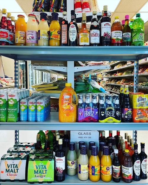 A shelf filled with various beverages, including juices, sodas, and alcoholic drinks, in a store setting.