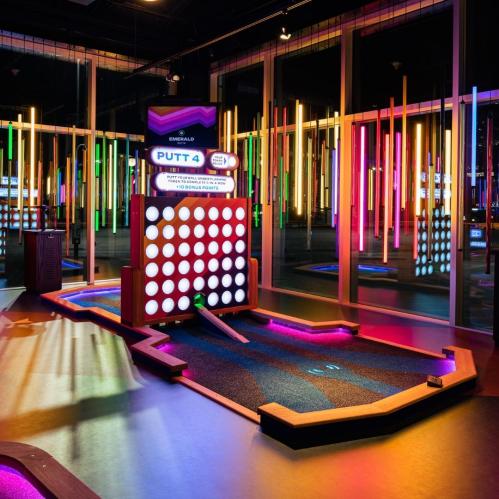A vibrant indoor mini-golf course with colorful lights and a unique putting challenge.