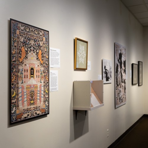A gallery wall featuring various artworks, including a colorful framed piece and informational plaques.