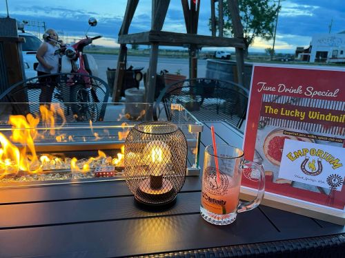 A cozy outdoor setting with a fire pit, a drink special sign, and a cocktail on a table at dusk.