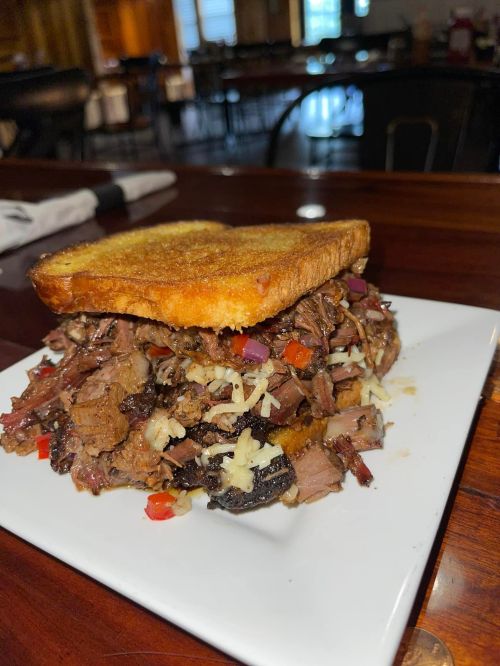 A hearty sandwich stacked with shredded beef, cheese, and diced vegetables, served on toasted bread.