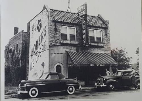 Black and white photo of a vintage ice cream shop with classic cars parked outside.