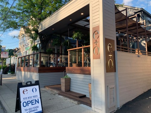 Exterior view of a modern restaurant with a patio, featuring a sign that says "OPEN" for to-go food and drinks.