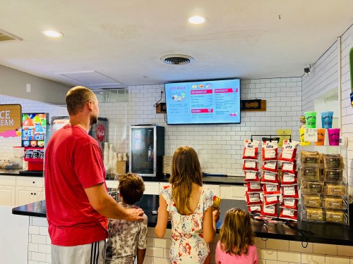 A family stands in front of a menu board at an ice cream shop, looking at their options.