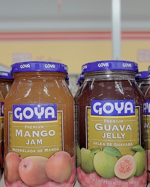 Two jars of Goya products: one labeled "Premium Mango Jam" and the other "Premium Guava Jelly," on a store shelf.