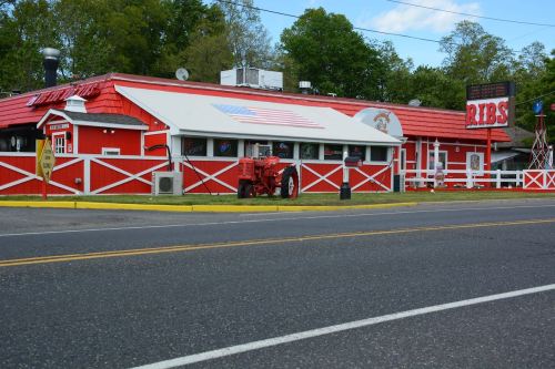 A red and white restaurant with a tractor outside, featuring a sign that says "Ribs," set along a roadside.