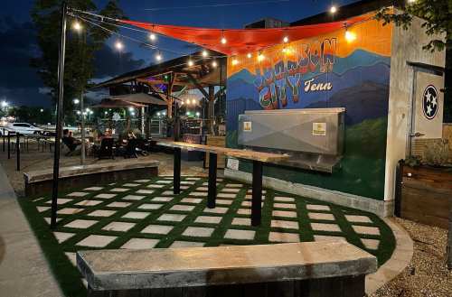 Outdoor dining area with benches, string lights, and a mural of "Jackson City, Tenn" on the wall.