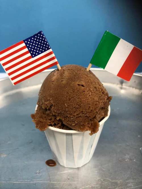 A cup of chocolate gelato topped with small flags of the USA and Italy.