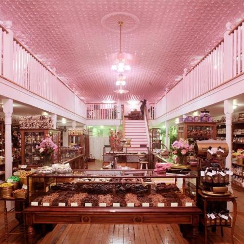 Charming chocolate shop with pink ceiling, wooden displays, and a variety of confections showcased in glass cases.