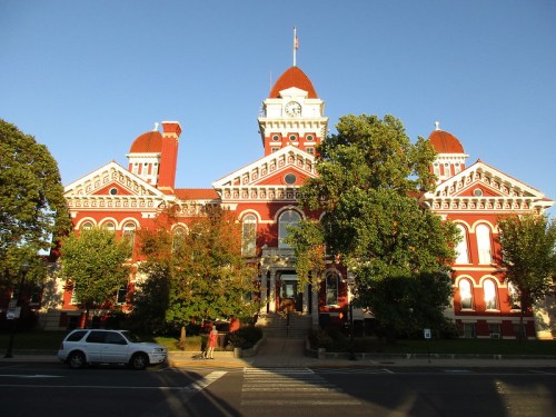 Historic red brick courthouse with ornate architecture, clock tower, and lush trees in front, under a clear blue sky.