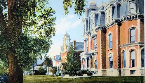 Historic brick buildings with ornate architecture, surrounded by lush greenery and trees under a clear blue sky.