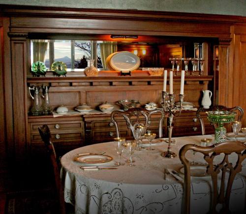 A vintage dining room with a wooden sideboard, elegant table settings, and a scenic view through large windows.