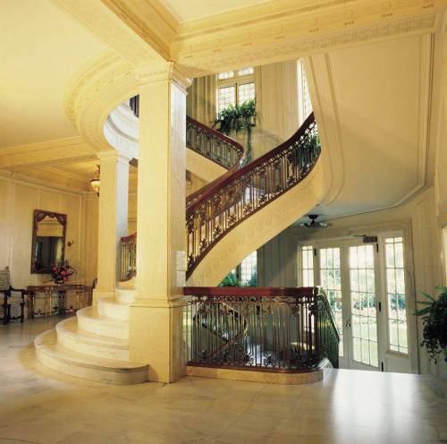 Elegant spiral staircase in a grand foyer, featuring ornate railings and natural light from large windows.