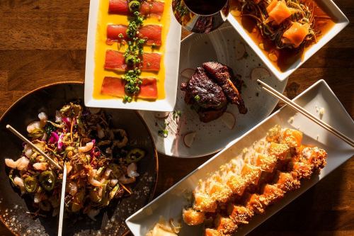 A vibrant spread of Asian dishes, including sushi, grilled chicken, and colorful salads, arranged on wooden table.