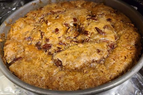 A freshly baked pecan pie in a round metal pan, with a golden-brown crust and visible pecan pieces on top.