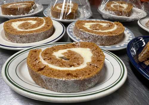 Slices of pumpkin roll cake with cream filling, displayed on plates and wrapped in plastic.