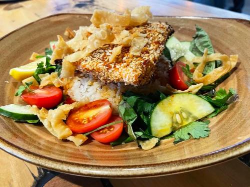 A plate of sesame-crusted fish on rice, garnished with fresh vegetables, herbs, and crispy fried onions.