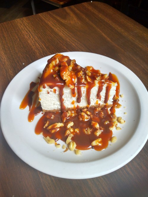 A slice of cake drizzled with caramel sauce and topped with chopped walnuts on a white plate.