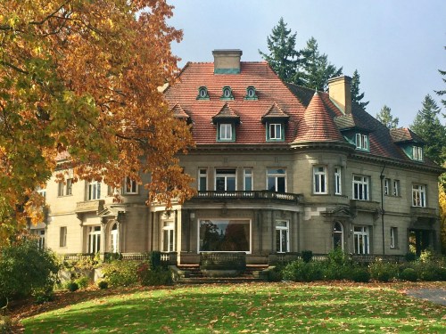 A grand, historic mansion surrounded by autumn foliage and a lush green lawn.