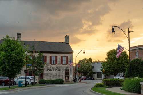 A quaint town street at sunset, featuring a historic building and American flags along the road.