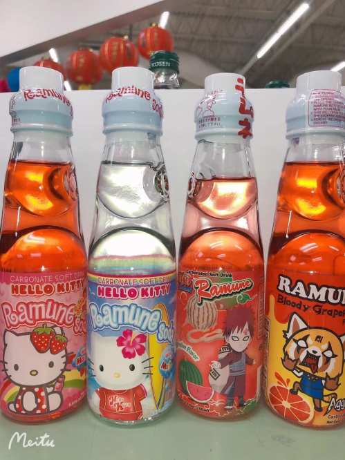 Four colorful bottles of Ramune soda featuring Hello Kitty and other character designs, with vibrant orange and pink hues.
