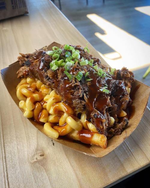 A serving of macaroni and cheese topped with pulled pork and barbecue sauce, garnished with green onions.