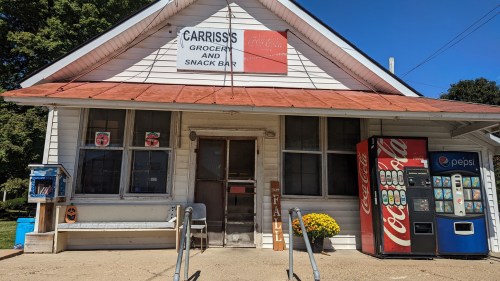 A small grocery and snack bar with a red roof, vending machines, and a welcoming entrance surrounded by greenery.