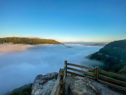 A scenic view of a fog-covered valley from a rocky overlook, with clear blue skies above.
