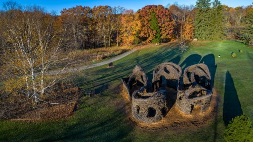 Aerial view of unique, large straw structures in a park surrounded by colorful autumn trees and a winding path.