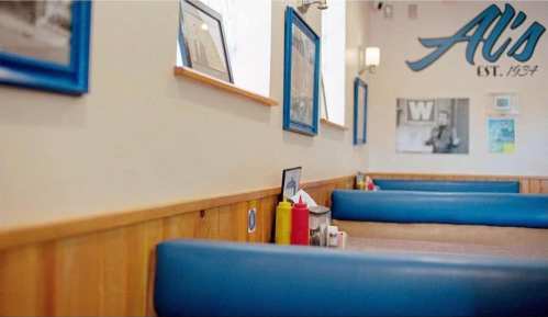 Interior of a diner featuring blue booths, framed photos, and condiment bottles on tables.